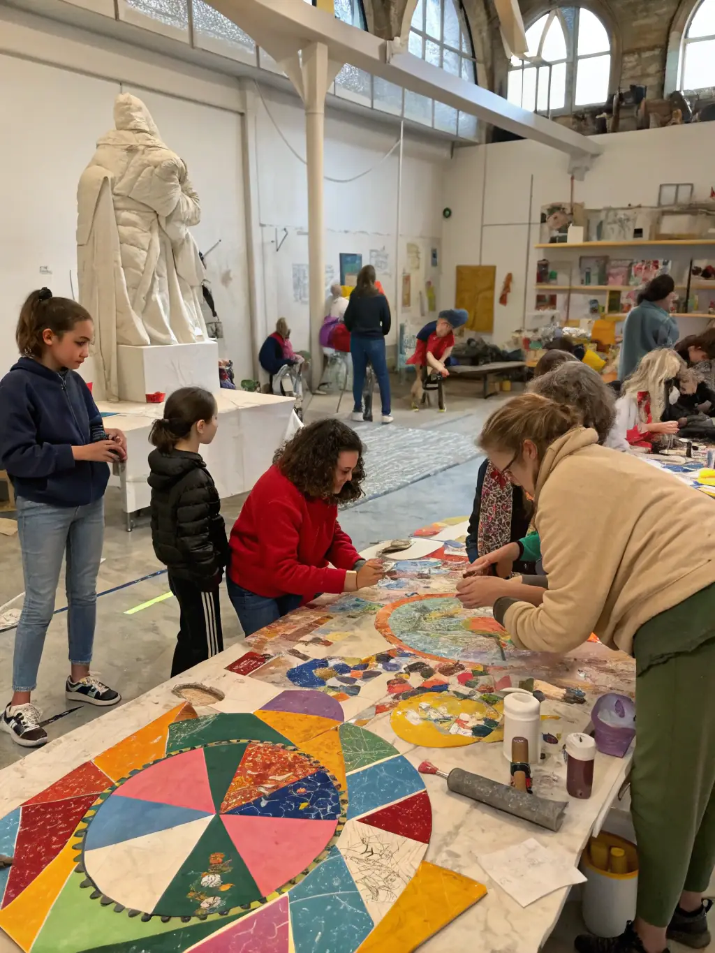 A photograph capturing a vibrant art workshop in progress at 26 LE HANGAR, with participants actively engaged in painting and sculpting, showcasing the organization's commitment to hands-on artistic learning.